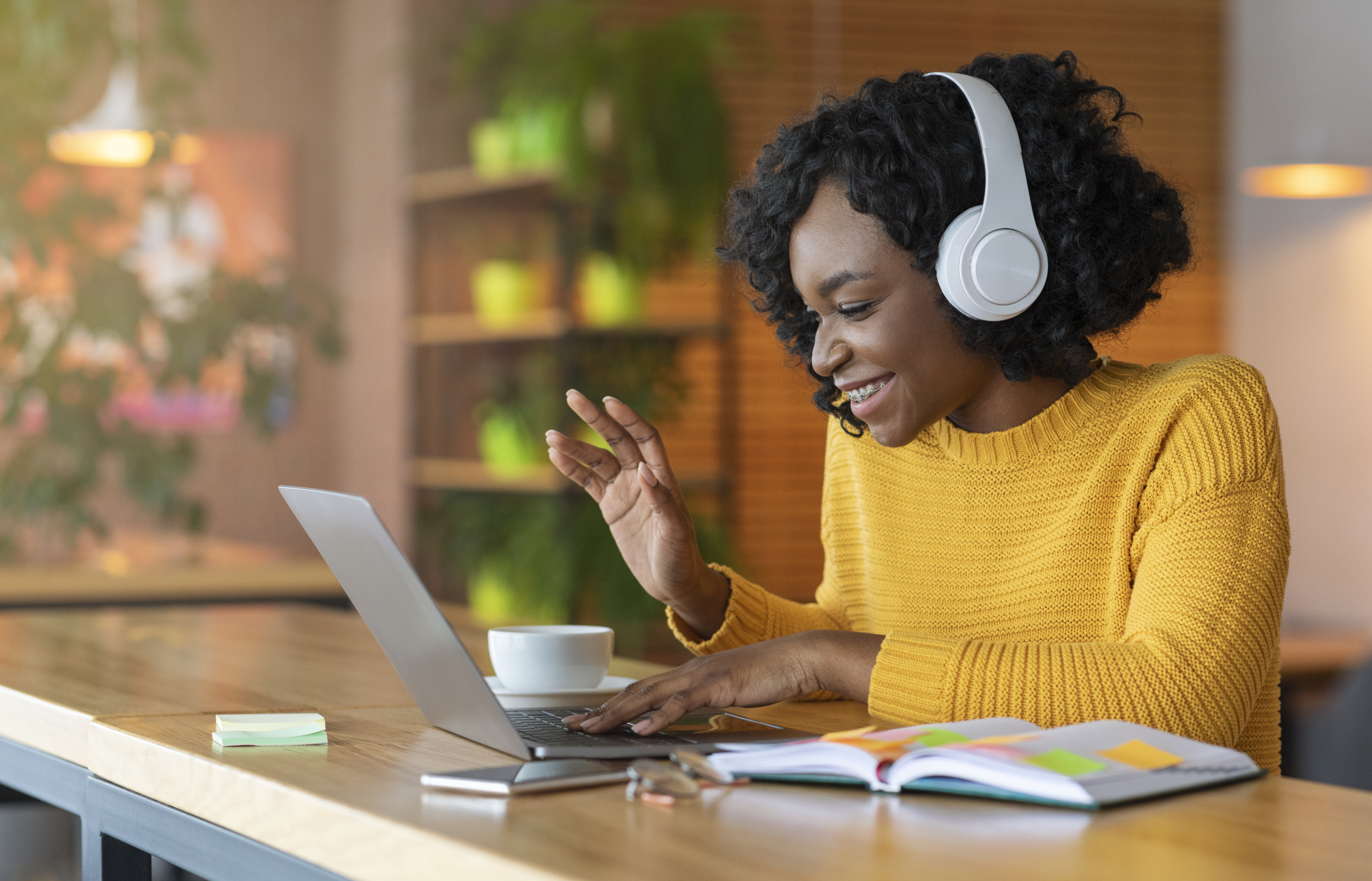 Woman wearing headphones and waving to laptop screen