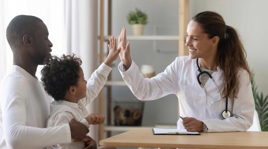 Doctor high-fives child on lap of his father.