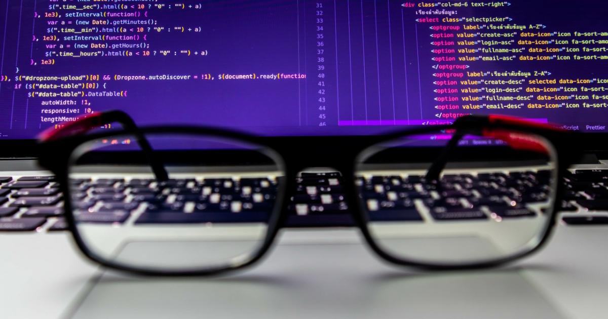 Glasses placed on the laptop with an open screen of program source code.