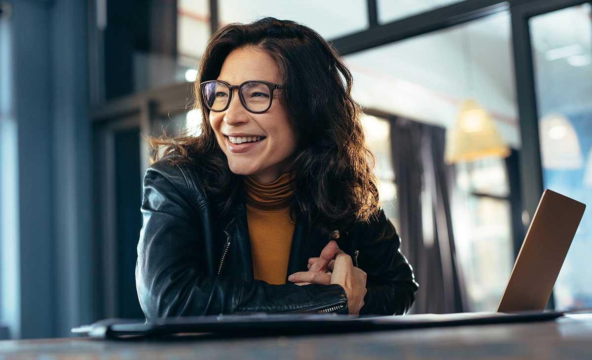 Young woman with glasses smiling in front of laptop.
